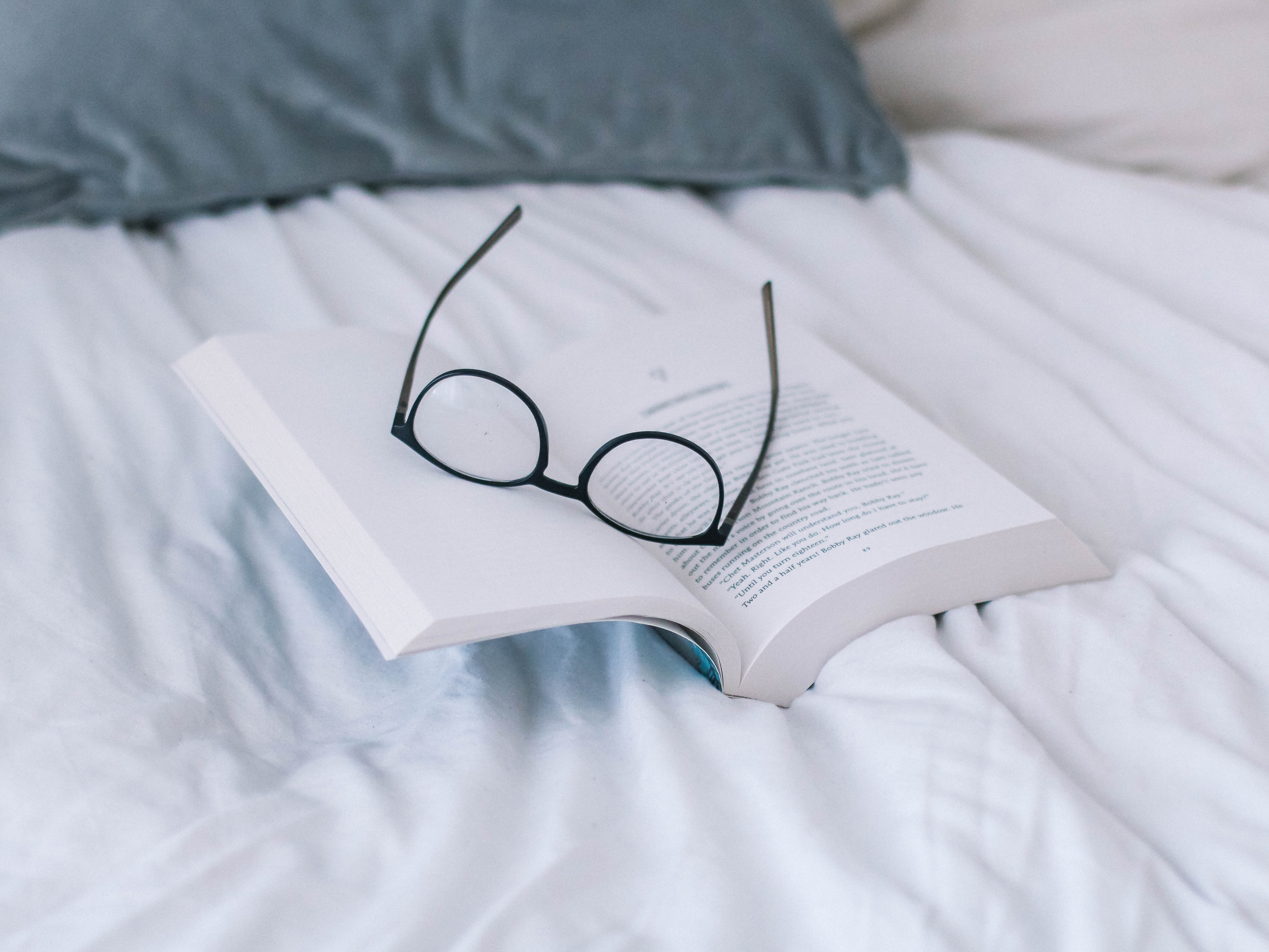 Book open on a bed with a pair of eye glasses keeping the book open
